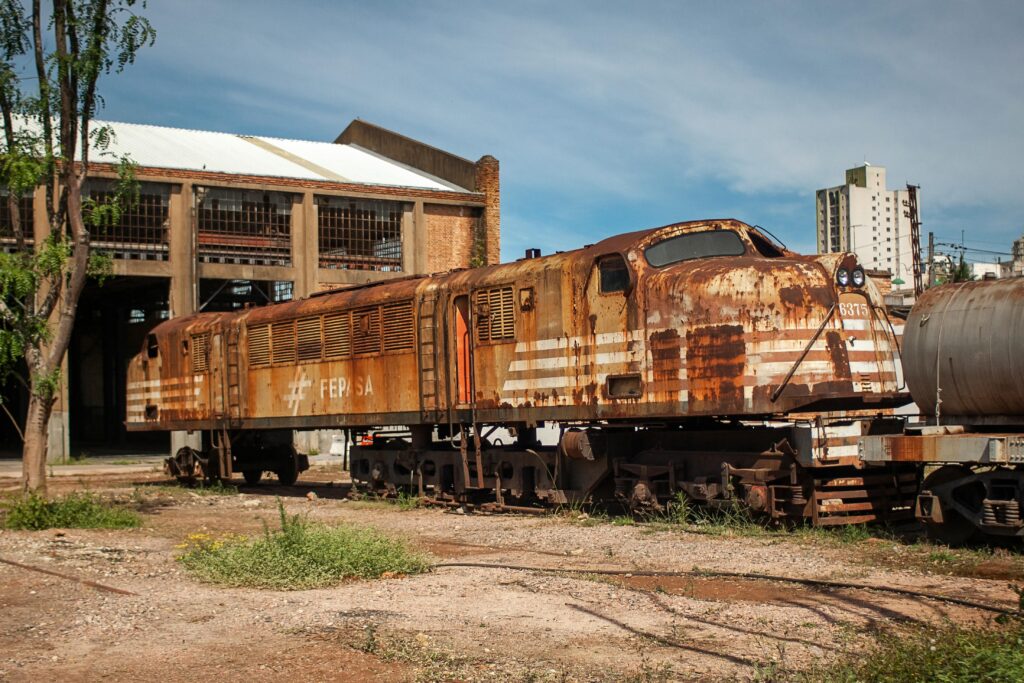 An old rusty train sits abandoned near a vintage warehouse in Brasil, capturing a historical and industrial vibe.