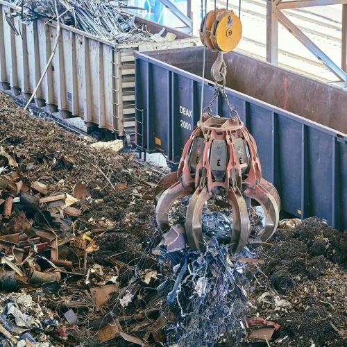 A claw crane lifting scrap metal in an industrial recycling facility.